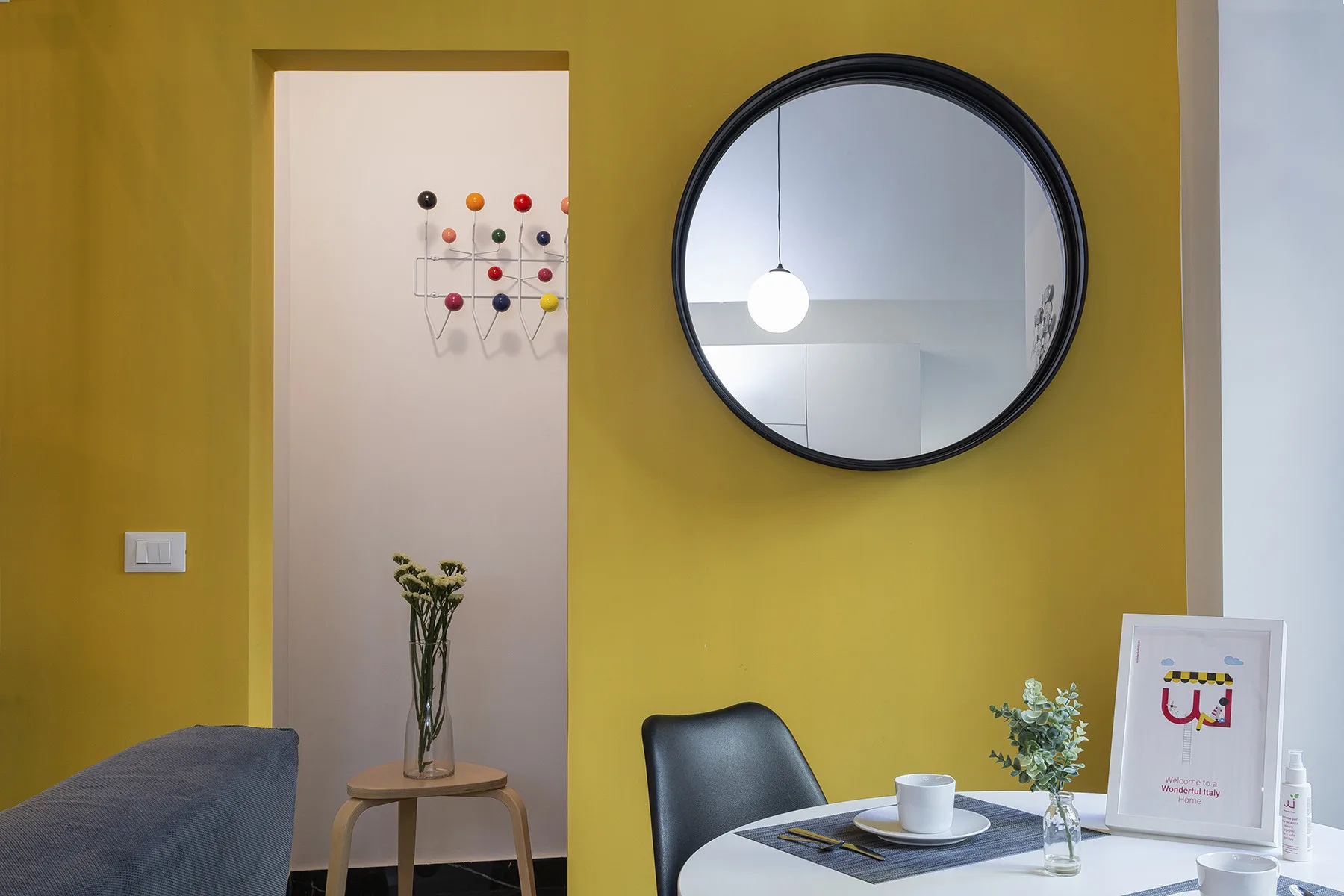 Un comedor con un espejo redondo en la pared y una mesa puesta frente a una pared amarilla.