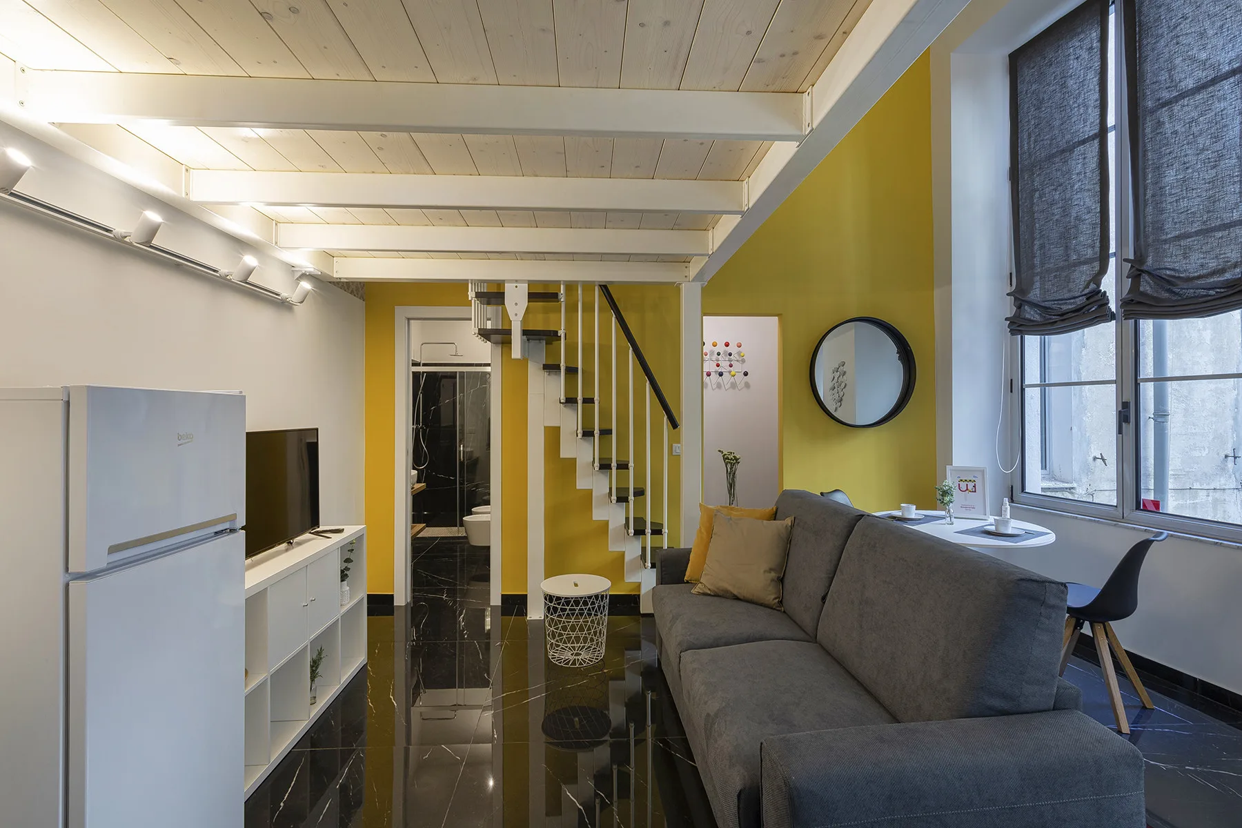 Una sala compacta con asientos grises junto a grandes ventanas y una escalera.