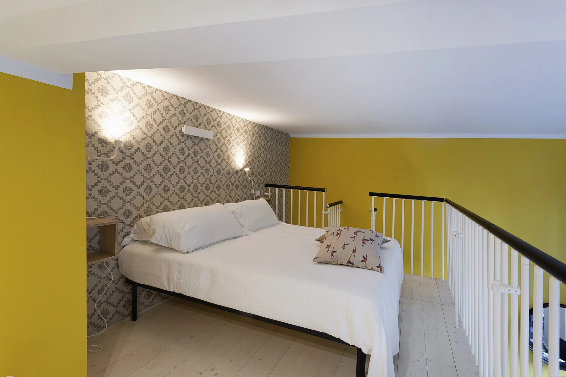 Zona de descanso con una cama junto a una barandilla y una pared estampada.