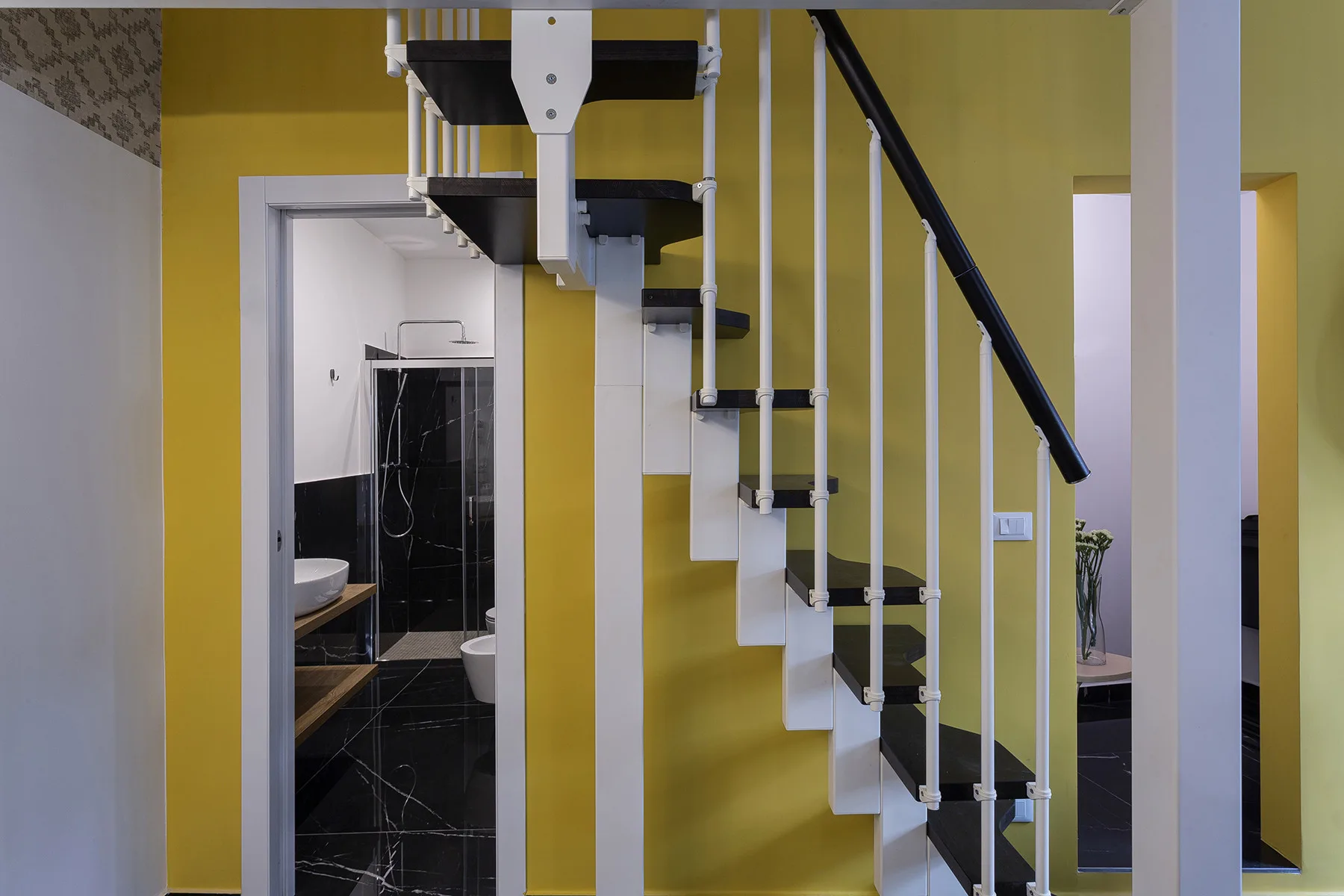Una escalera con peldaños blancos y barandales negros está junto a la entrada de un baño.