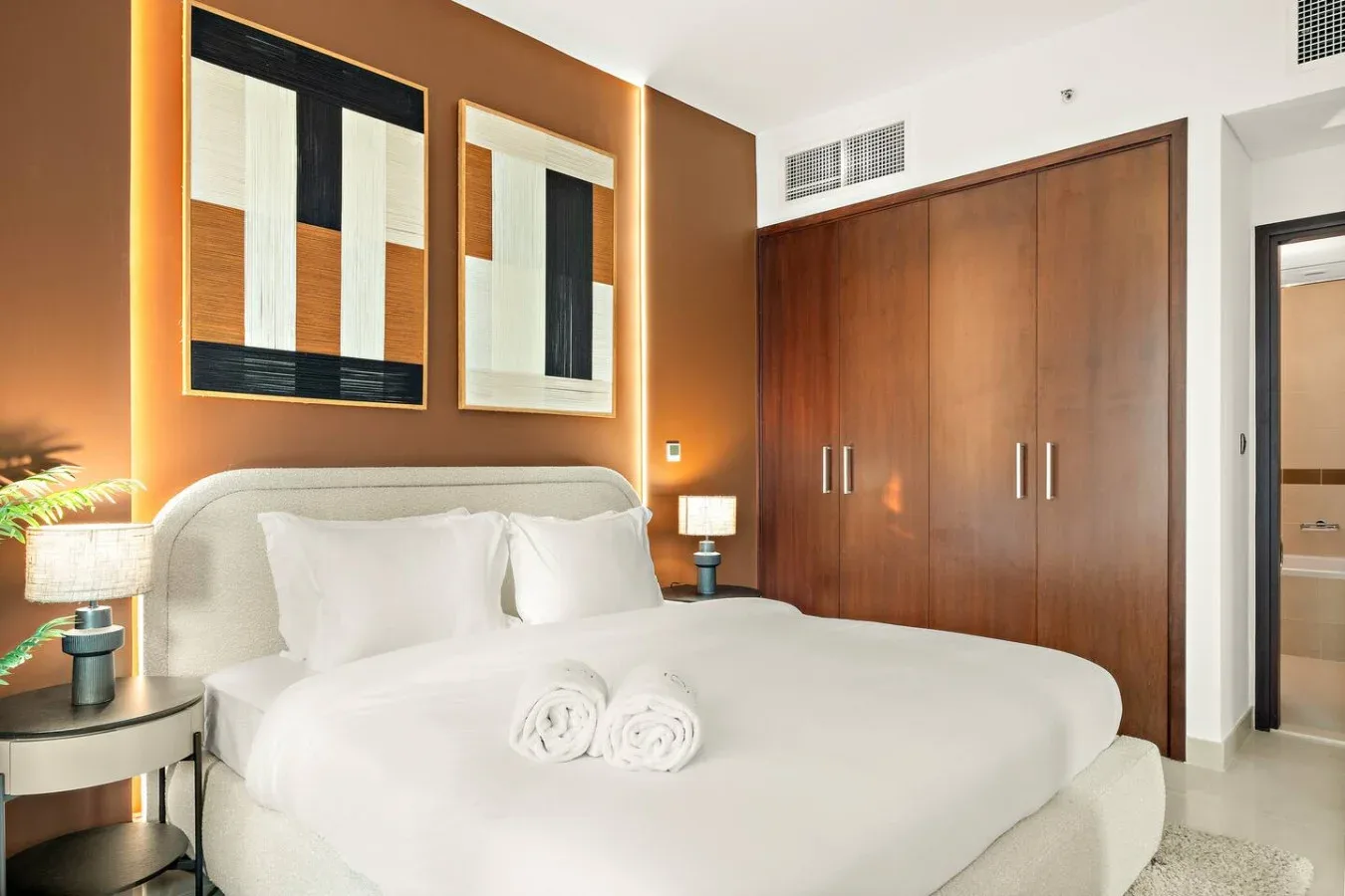 Un dormitorio con una cama tendida bajo cuadros abstractos enmarcados.