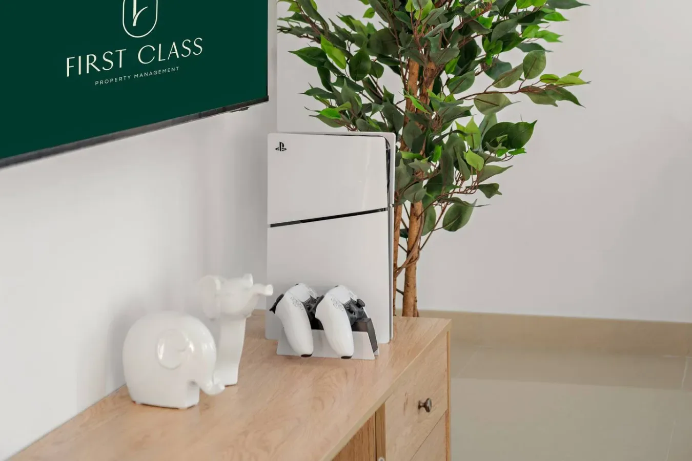 Una consola muestra dispositivos de videojuegos junto a una planta de interior frondosa.