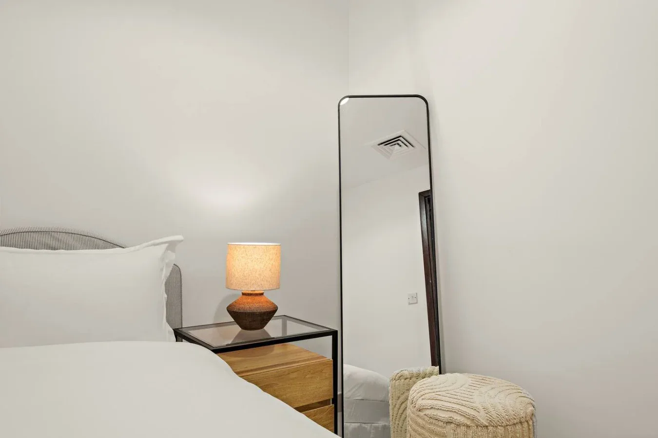 Un dormitorio con una cama, una lámpara de noche y un espejo de cuerpo entero.