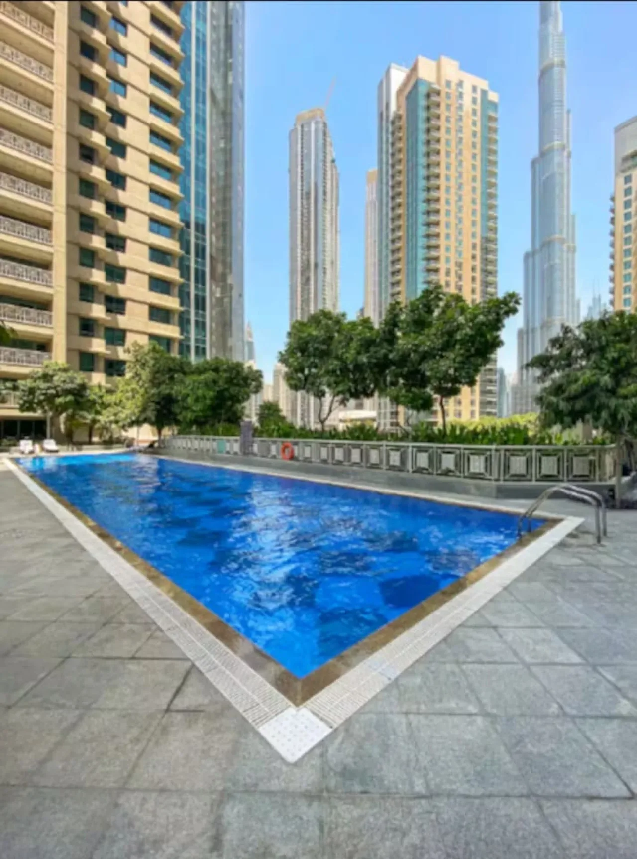 Una piscina al aire libre está rodeada de edificios altos y árboles.