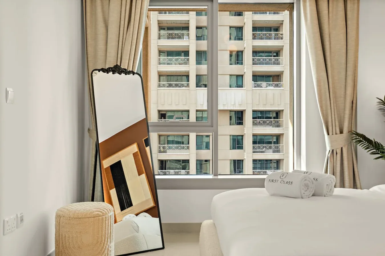 Un dormitorio con una cama junto a una ventana grande con vista a un edificio vecino.