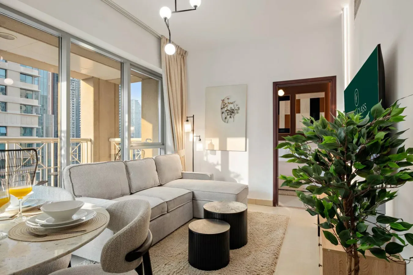 Una sala luminosa con sofá seccional, grandes ventanas y una planta frondosa.