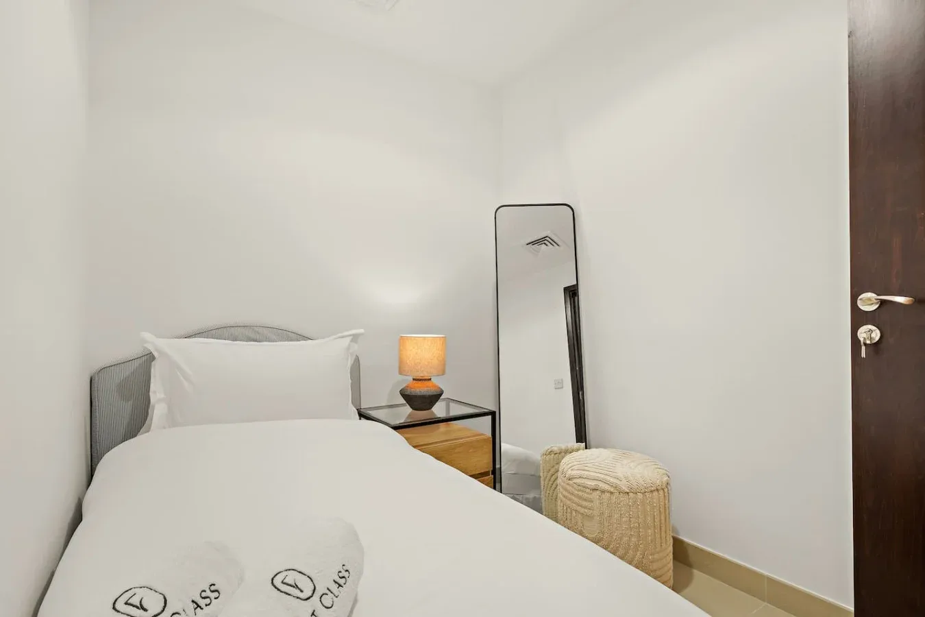 Un dormitorio con una cama tendida, una mesita de noche y un espejo de cuerpo entero.