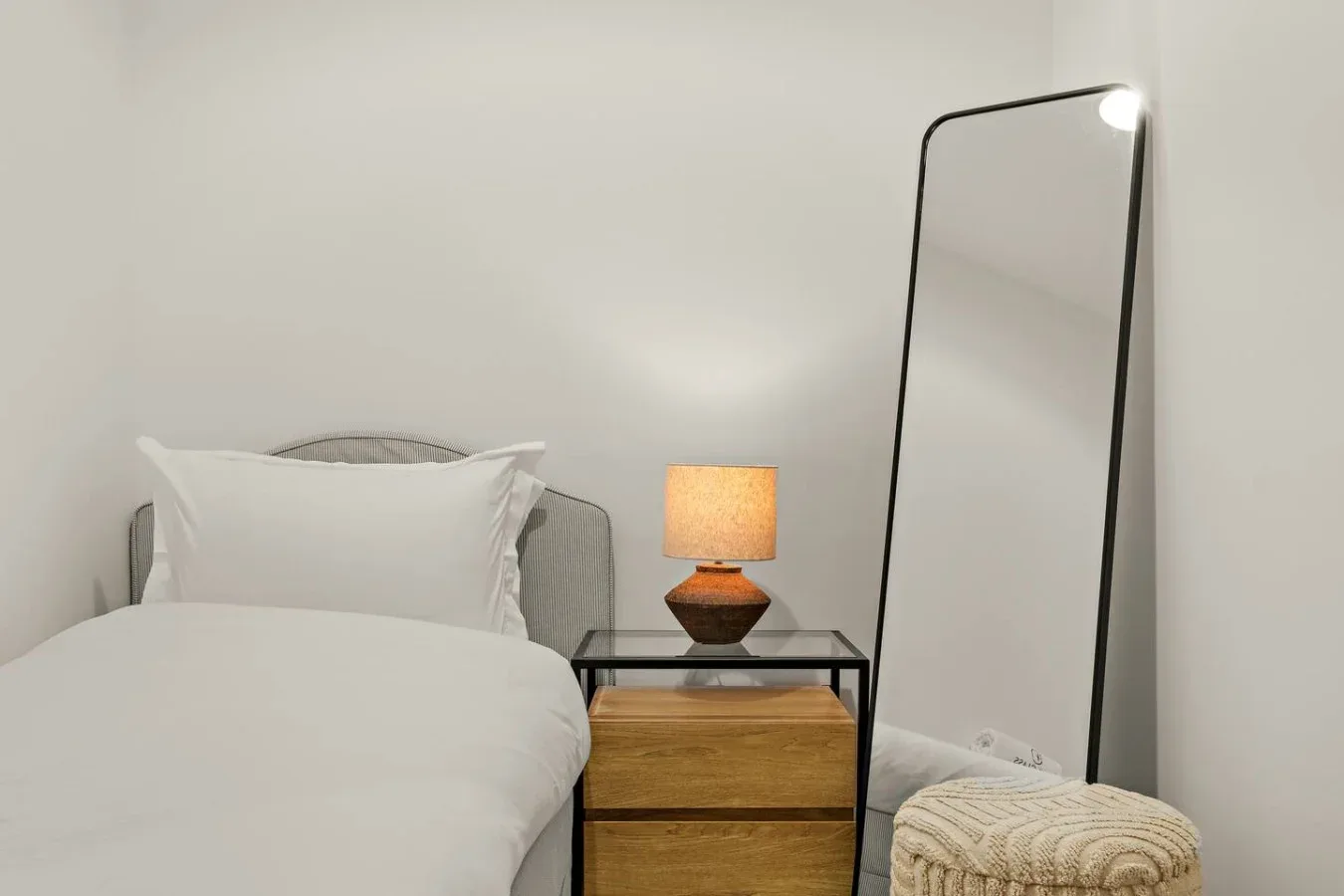 Un dormitorio con una cama, una mesita de noche y un espejo de cuerpo entero.