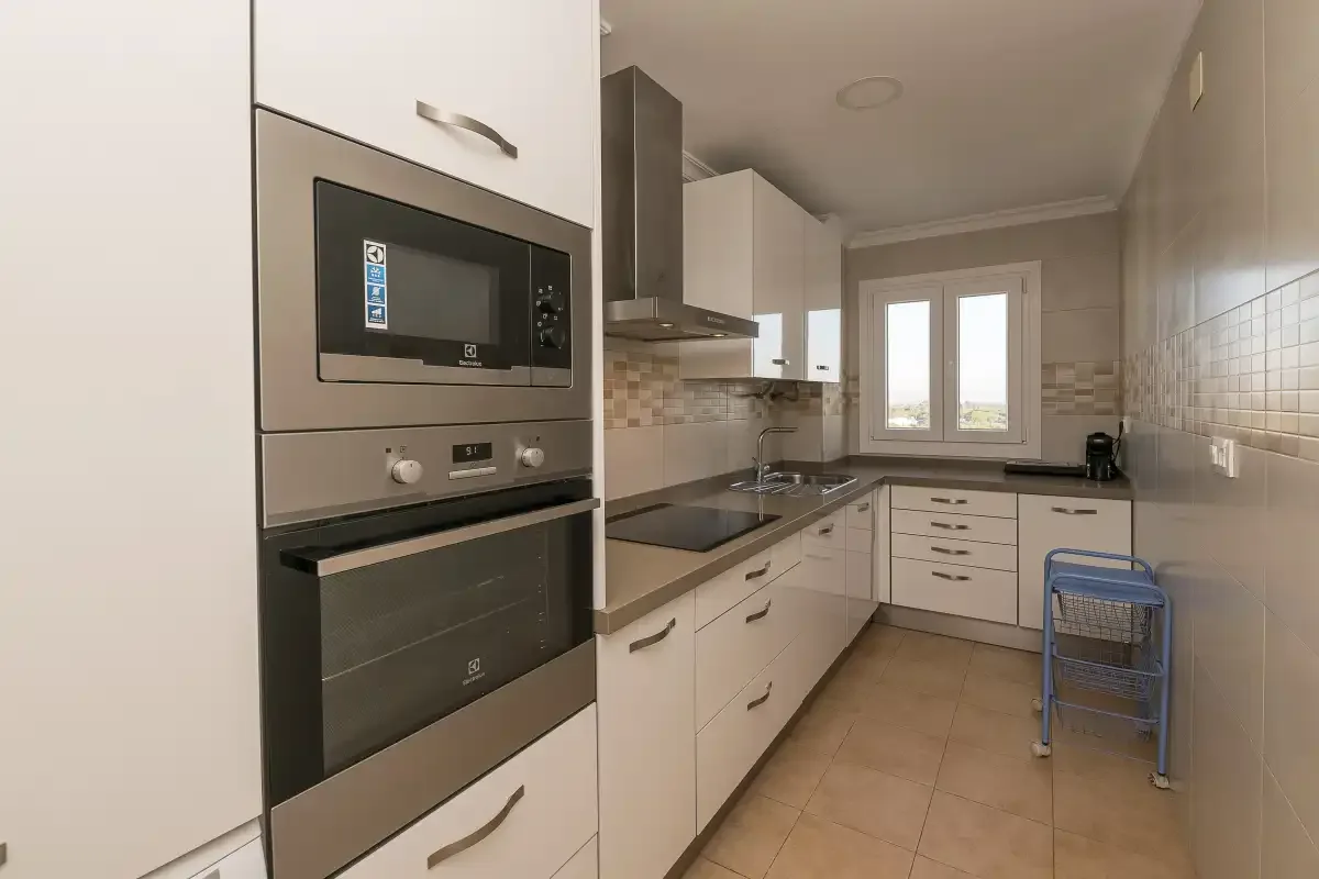A modern kitchen with white cabinets, built-in appliances, and a window.