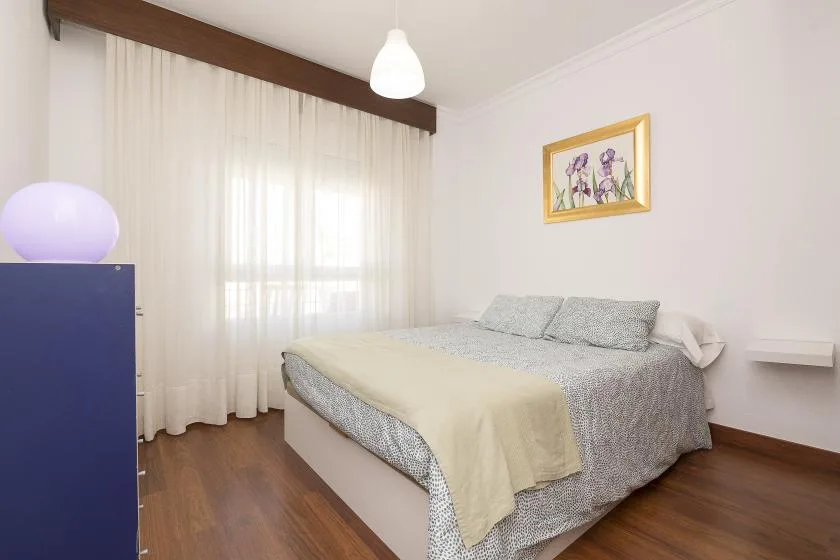 Bedroom with a bed beside a large curtained window.
