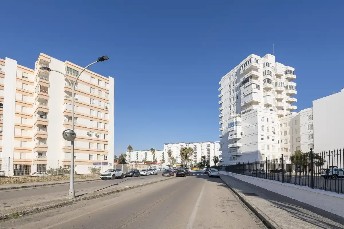 An urban street runs between apartment buildings under a clear blue sky.