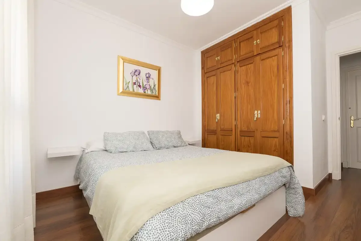 A bedroom with a bed, wooden wardrobe, and framed floral artwork.