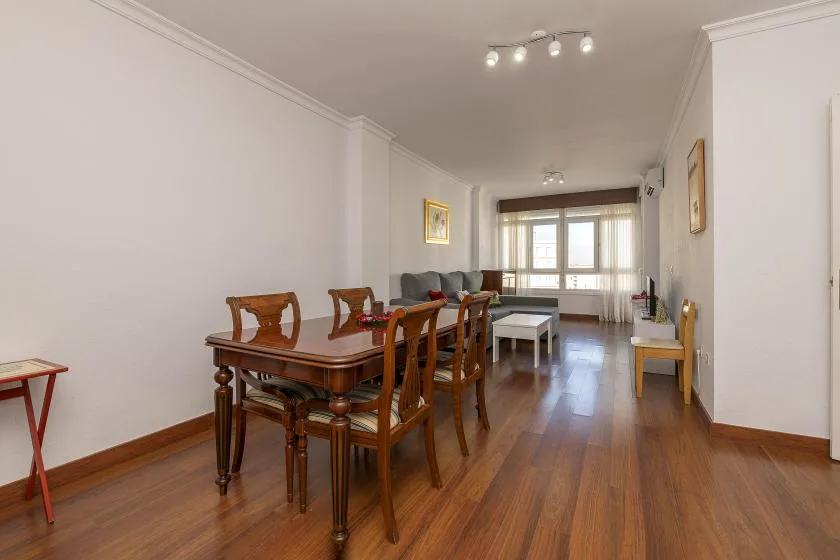 A dining and living room with a wooden table and seating near the windows.