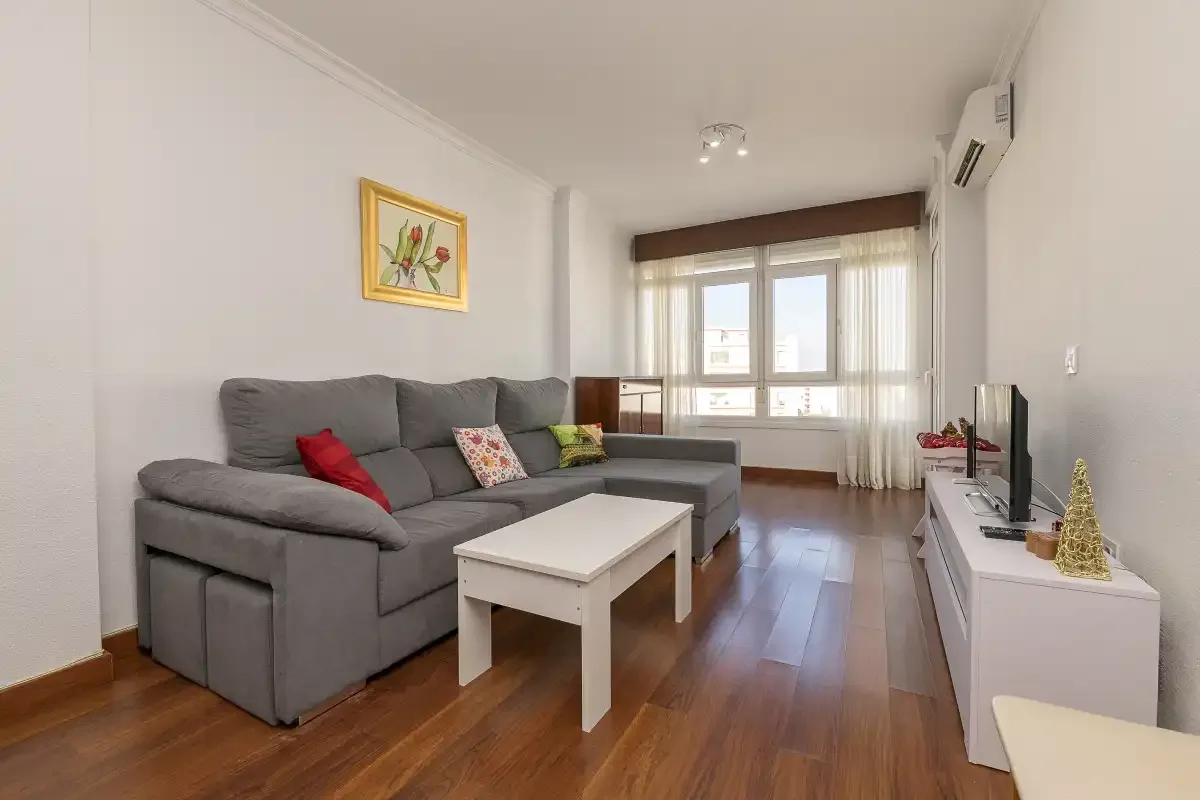 A living room with a gray sectional, white coffee table, and large windows.