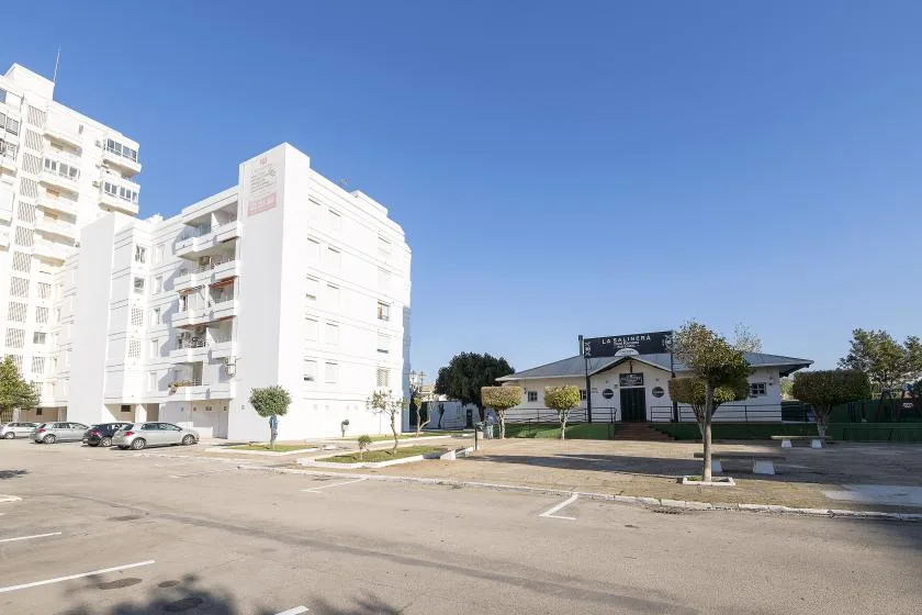 A residential street with white apartment buildings and a low building beneath a clear blue sky.