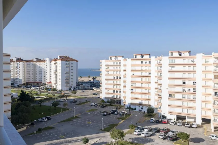 View of apartment buildings, a parking area, and the sea in the distance.
