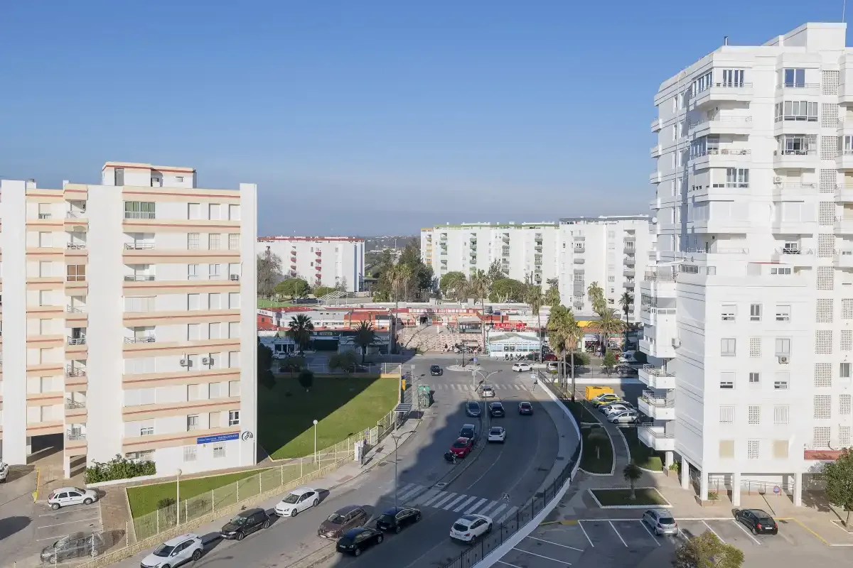 A city street curves between apartment buildings under a clear blue sky.