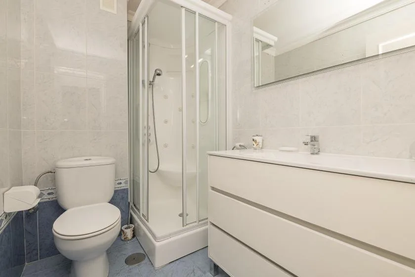 A bright bathroom with a glass shower, toilet, and long vanity.