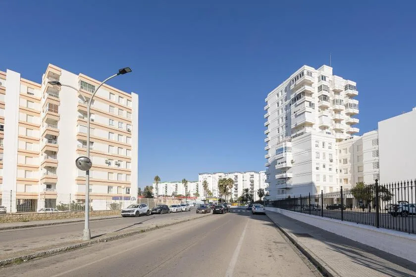 A city street runs between apartment buildings beneath a clear blue sky.