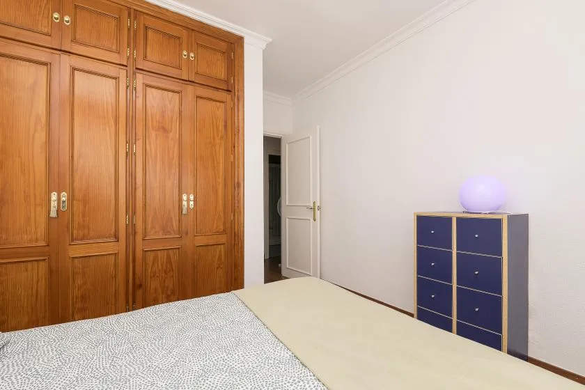 A bedroom with wooden wardrobes, a bed, and a blue chest of drawers.