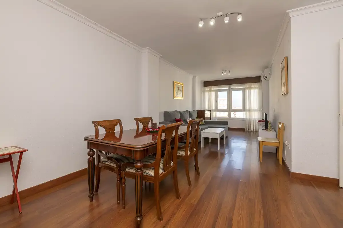 A dining and living room with a wooden table and seating by the windows.