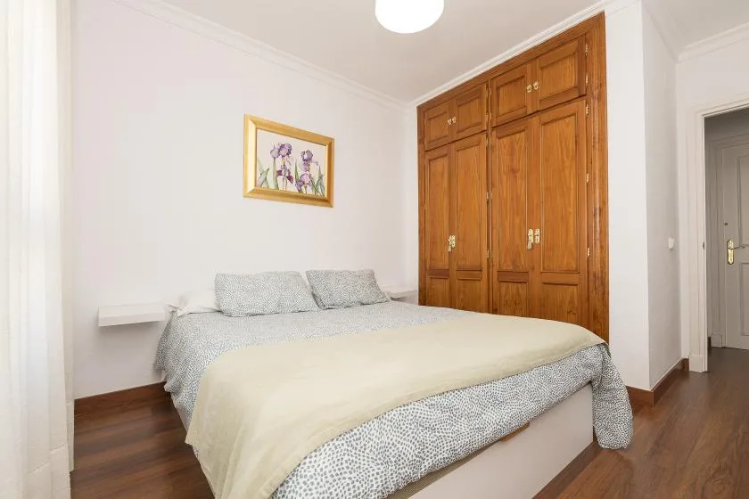 A bedroom with a bed, wooden built-in cabinets, and a framed floral picture.