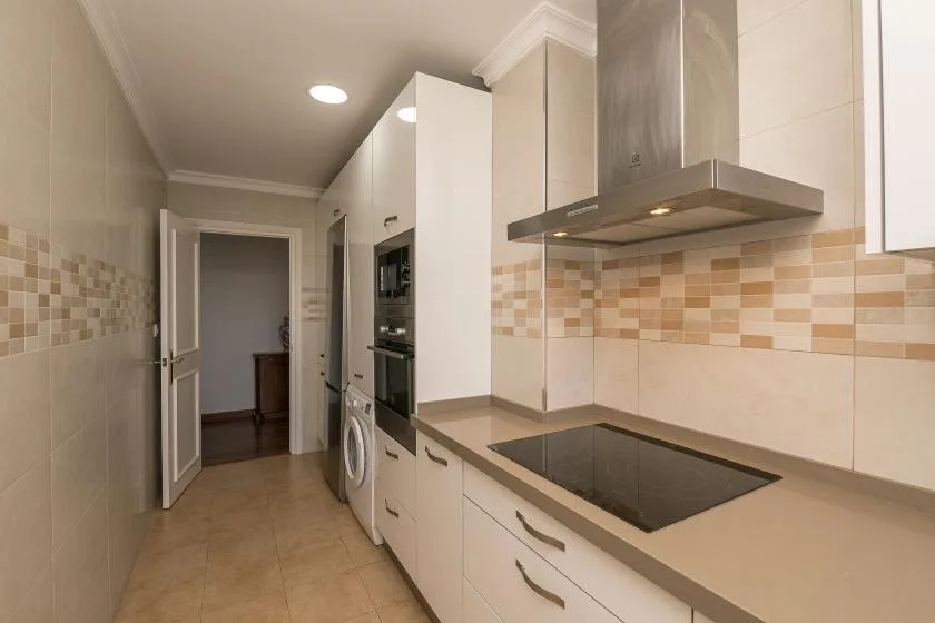A narrow kitchen with a countertop cooktop, range hood, and built-in appliances.