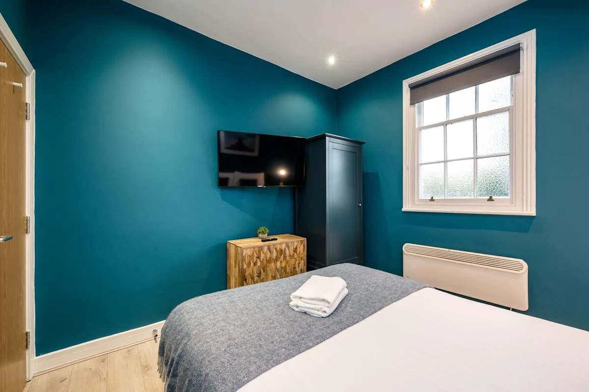 A bedroom with a bed, wall-mounted television, and window.