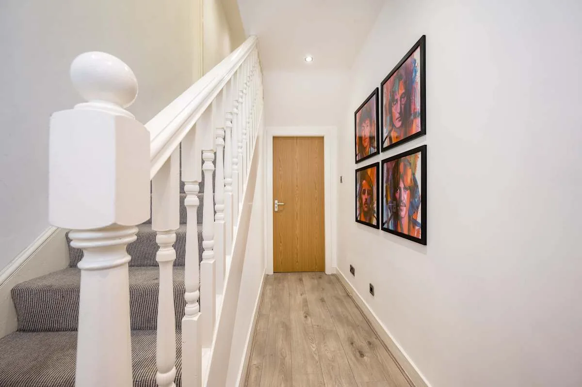 A narrow hallway with a staircase, framed artwork, and a wooden door.