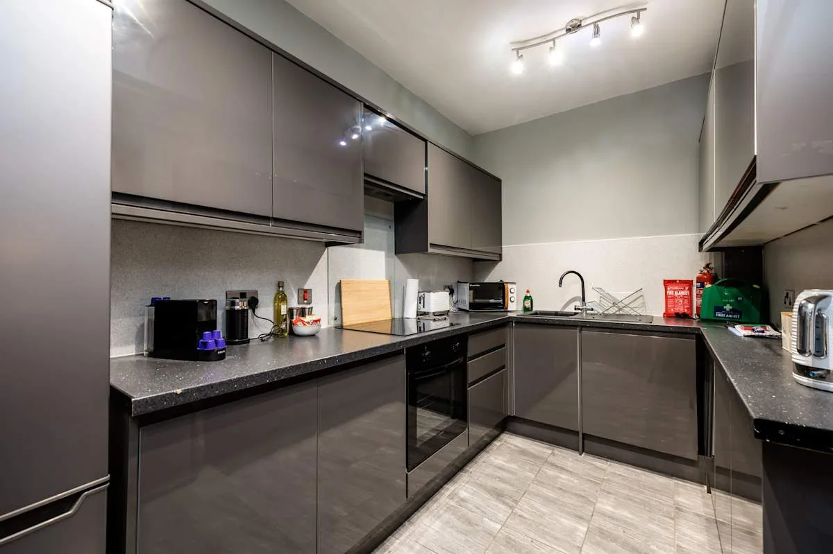 A modern kitchen with dark cabinets, countertops, and a sink.