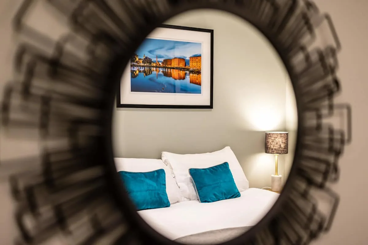 Bedroom with a neatly made bed and framed waterfront artwork.