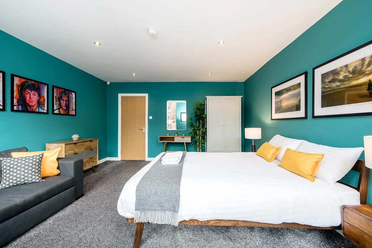 A bedroom with a large bed, teal walls, and framed artwork.