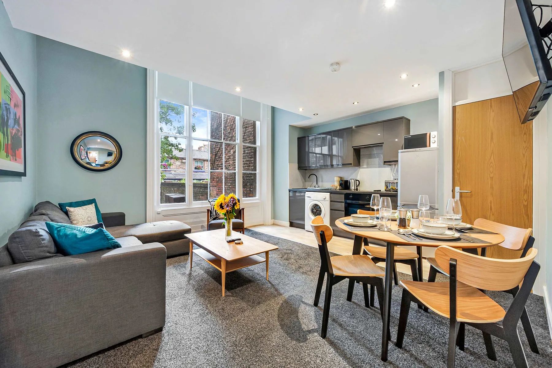 A living and dining area opens into a compact kitchen, with large windows nearby.