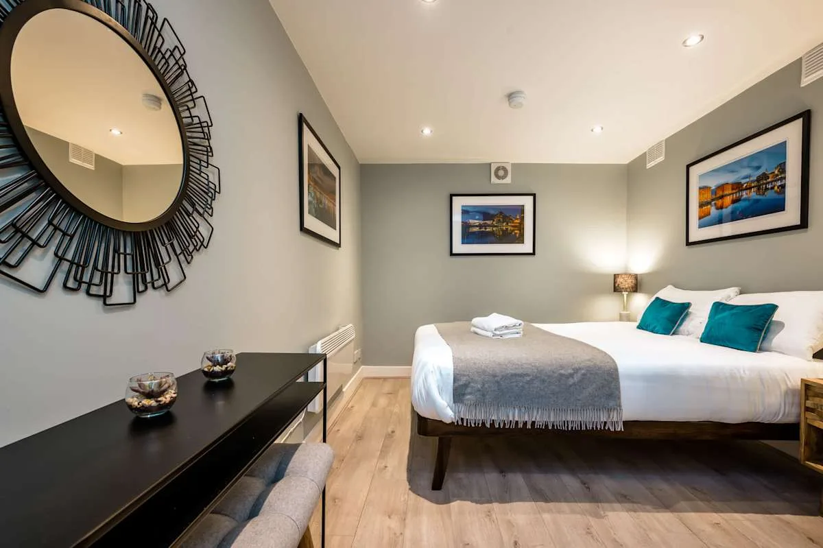 A bedroom with a neatly made bed, turquoise pillows, and framed pictures.