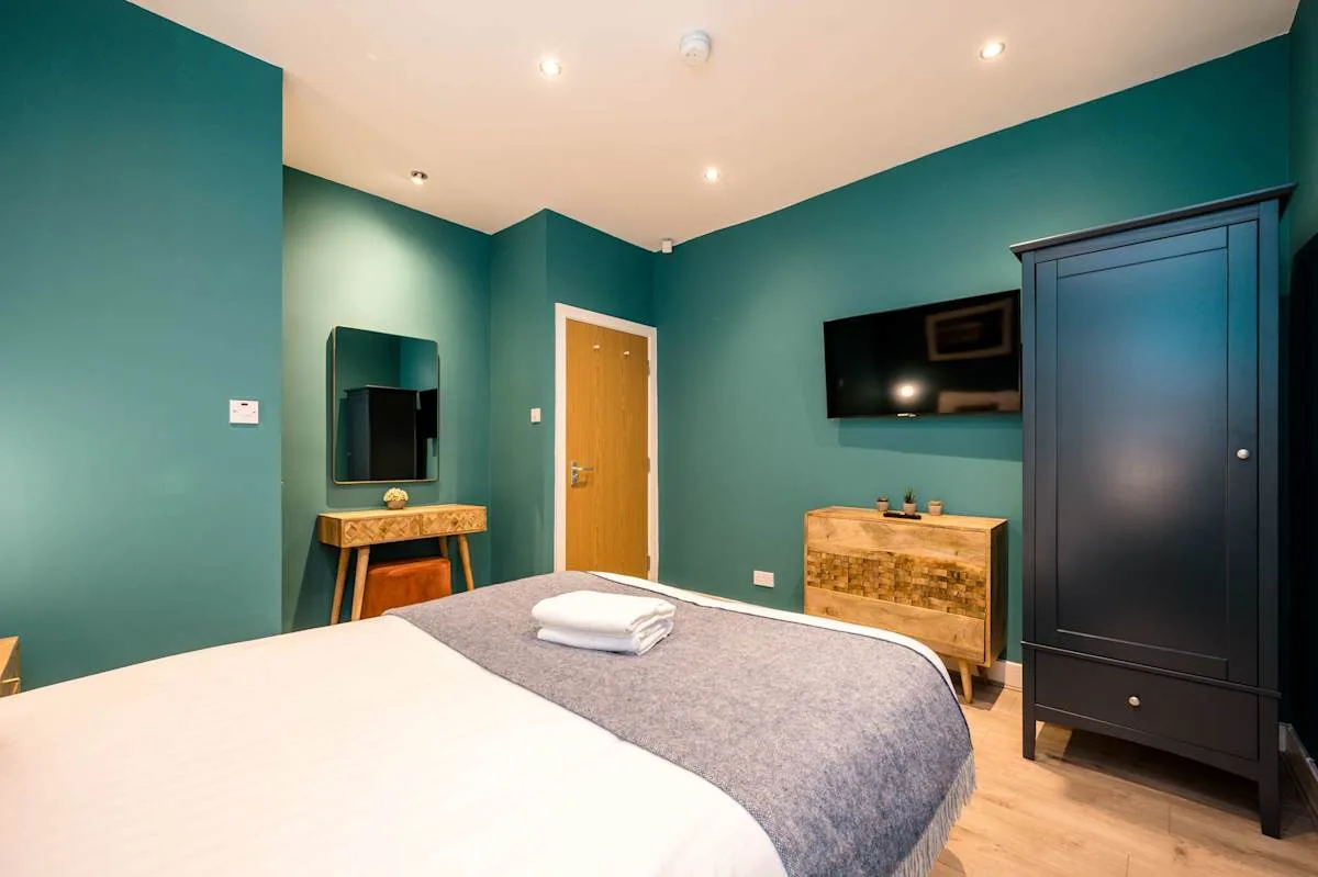 A bedroom with a bed, teal walls, and a television mounted above a dresser.