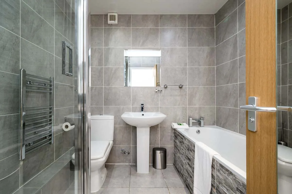A tiled bathroom with a bathtub, pedestal sink, and toilet.