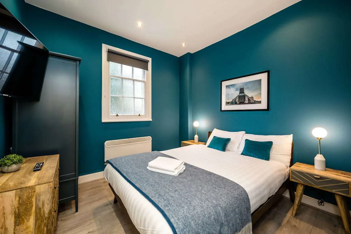 A bedroom with a neatly made bed, teal walls, and bedside lamps.