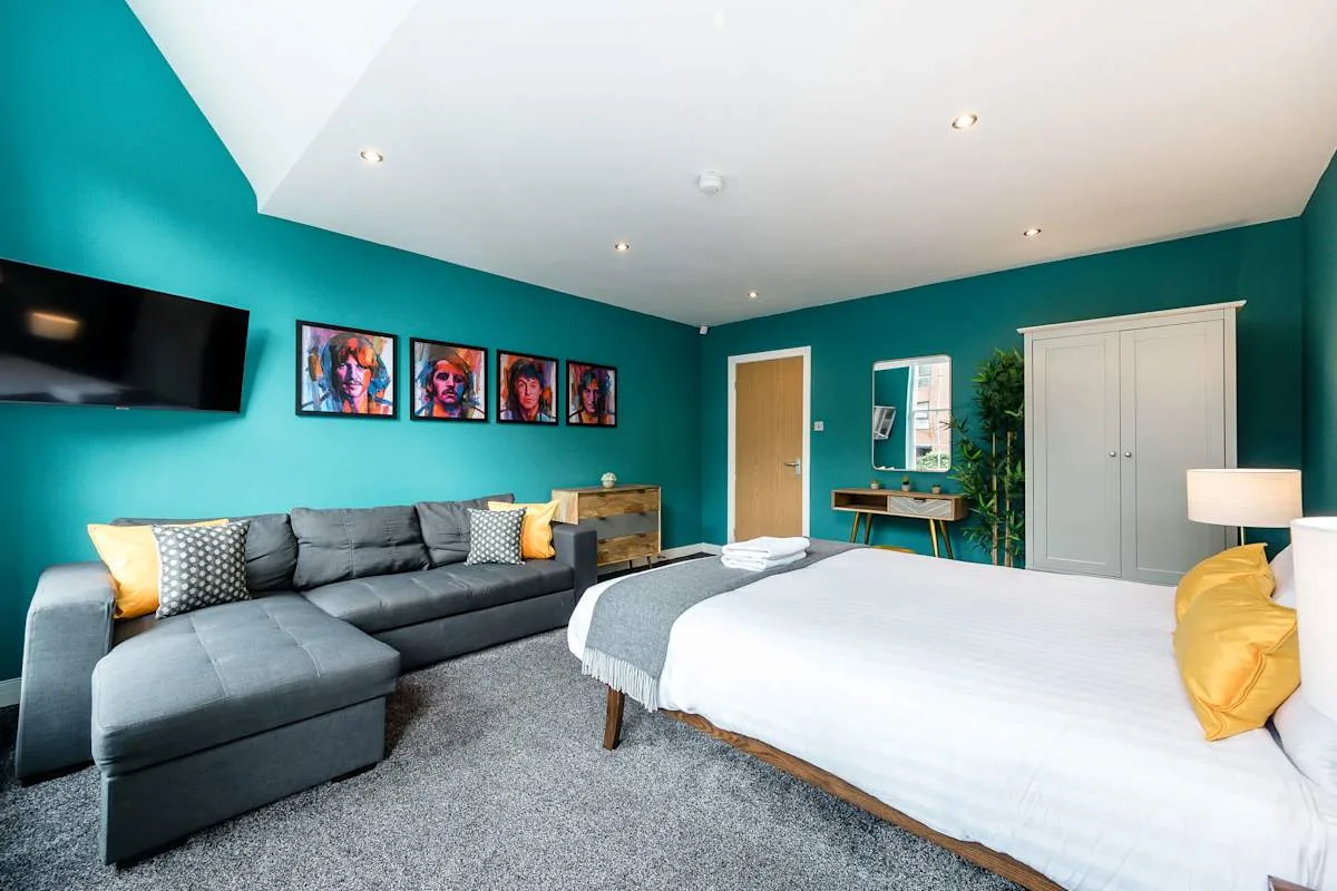 A bedroom with a large bed, gray seating, and teal walls.