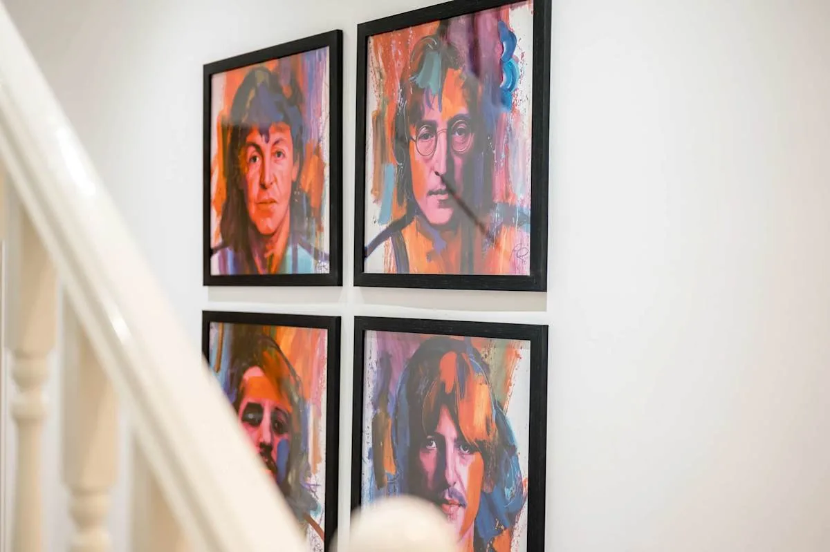 A wall displays four colorful framed portraits beside a staircase.