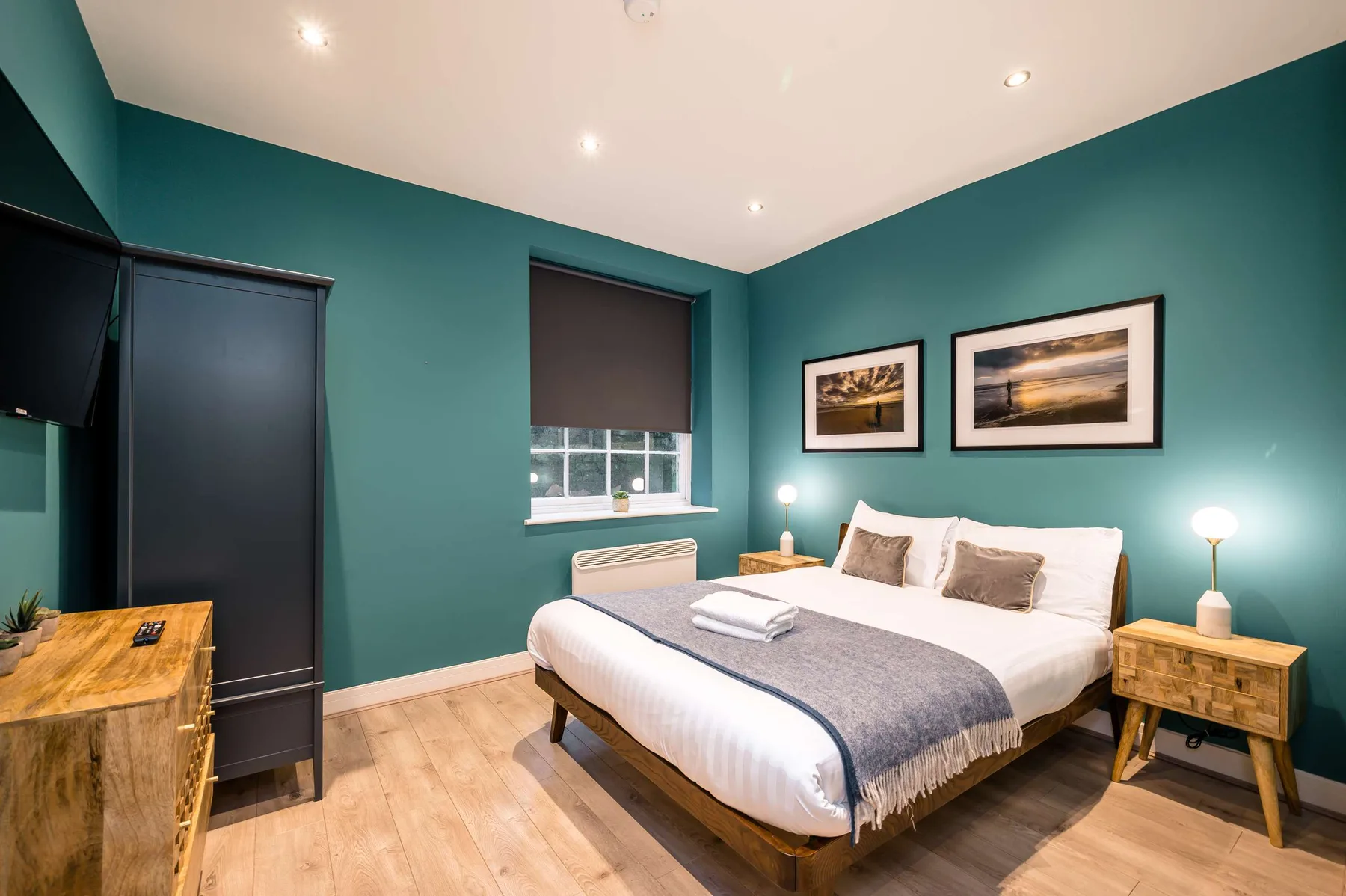 A bedroom with a bed, teal walls, and framed pictures.