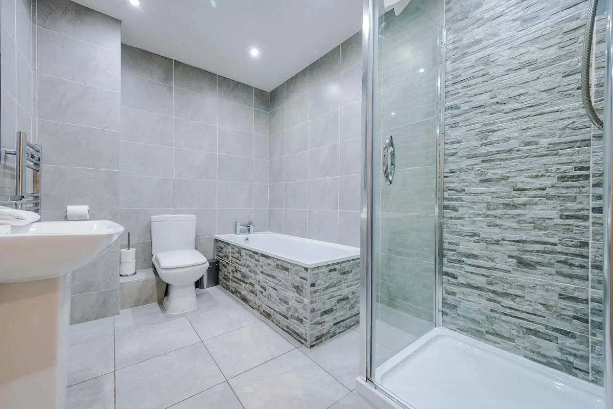 A tiled bathroom with a bathtub, toilet, sink, and glass shower.