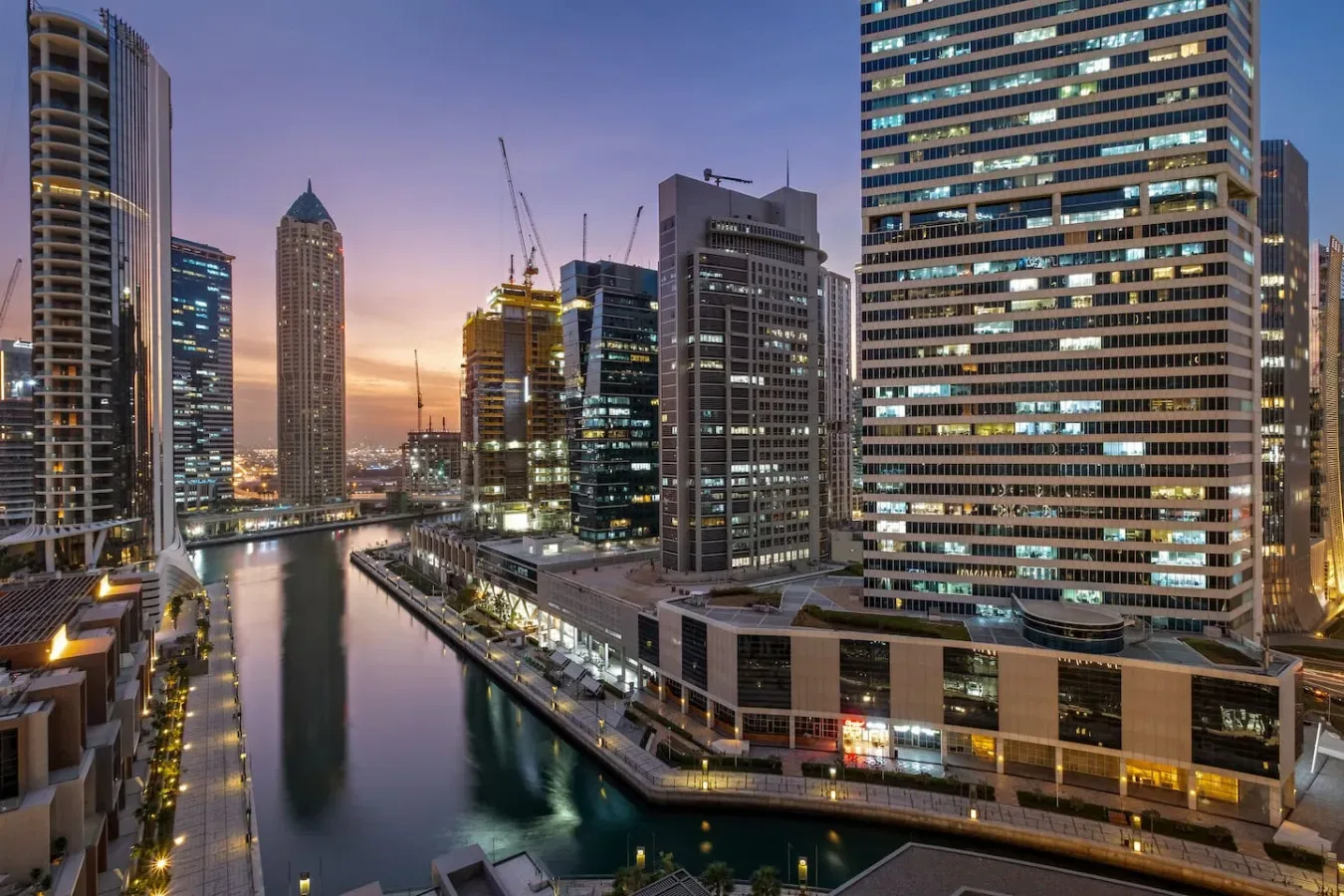 Un canal urbano pasa entre edificios altos iluminados al anochecer.