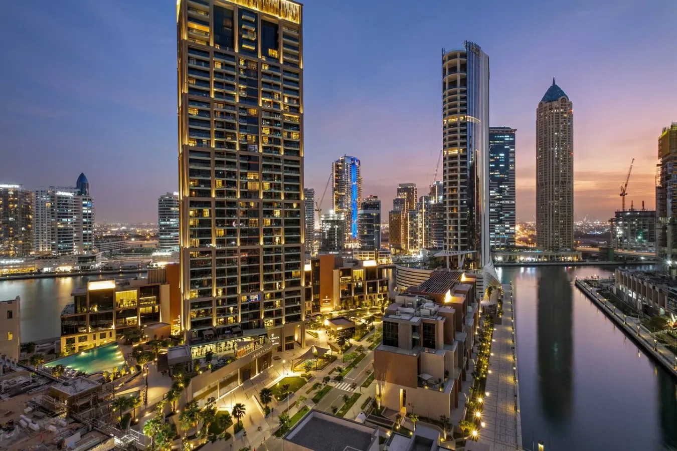 El horizonte urbano al atardecer se alza junto a un canal tranquilo y edificios iluminados.