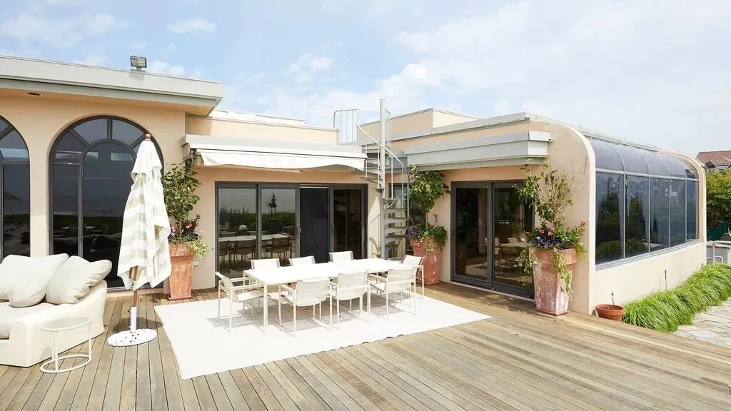 A rooftop terrace with outdoor seating beside a glass-enclosed sunroom.