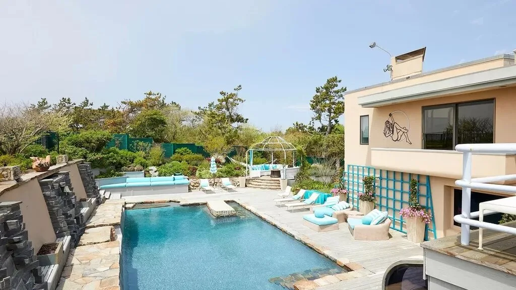 An outdoor swimming pool beside a modern building, with lounge seating around the deck.