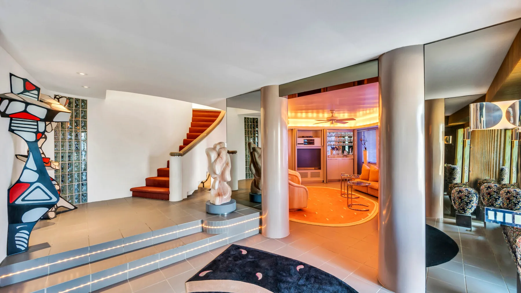 A modern interior with a colorful sculptural figure beside steps and a warmly lit sitting area.