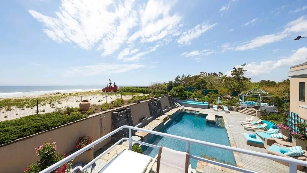 An outdoor poolside terrace overlooks a sandy beach and the ocean.