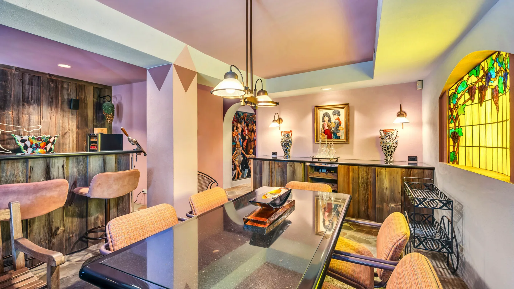 A dining area with a long table, seating, and a colorful stained-glass window.