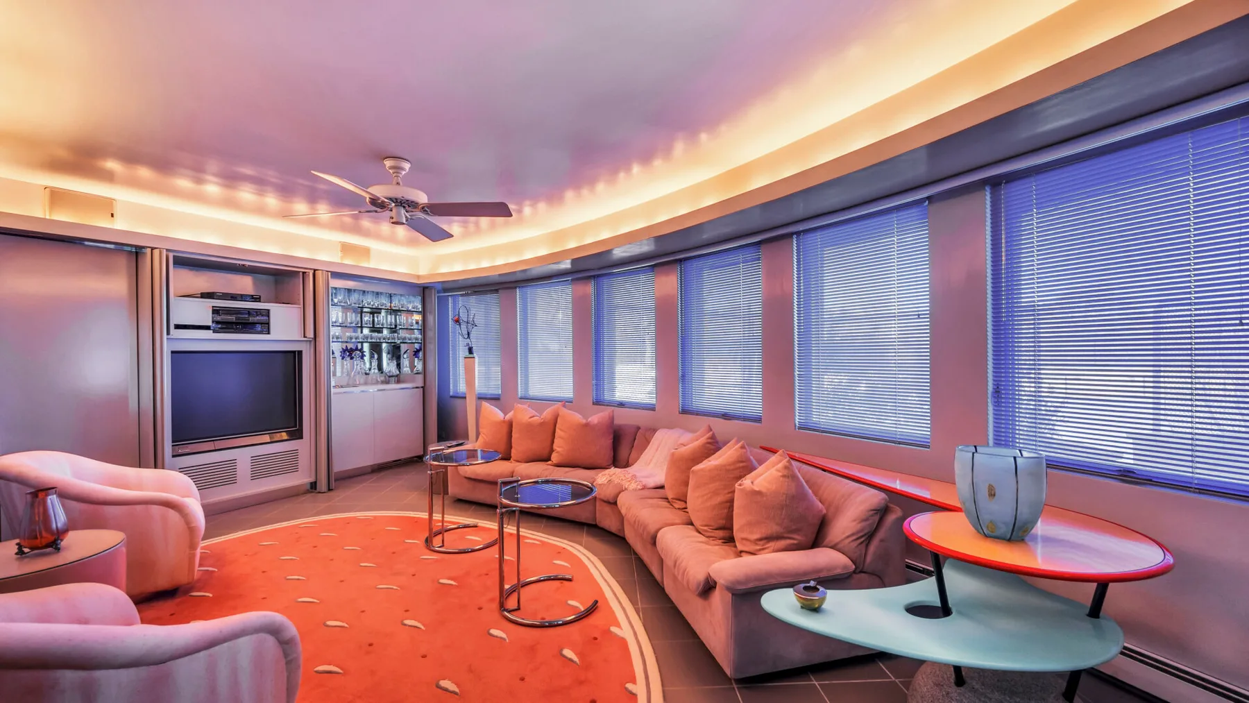 A living room with curved seating, several windows, and a television.