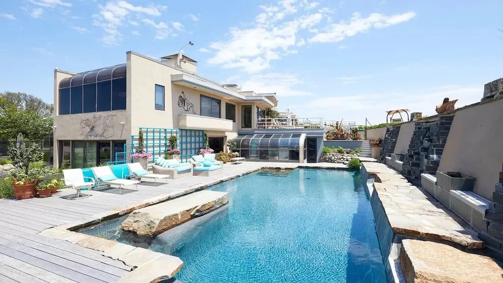 A modern house overlooks a swimming pool with a paved deck.